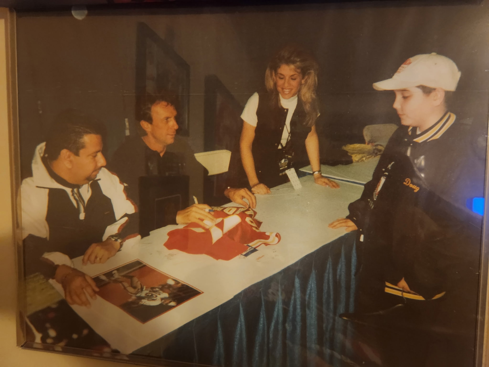 A young Doug Mankiewicz watches Joe Montana sign his jersey at a card show signing table